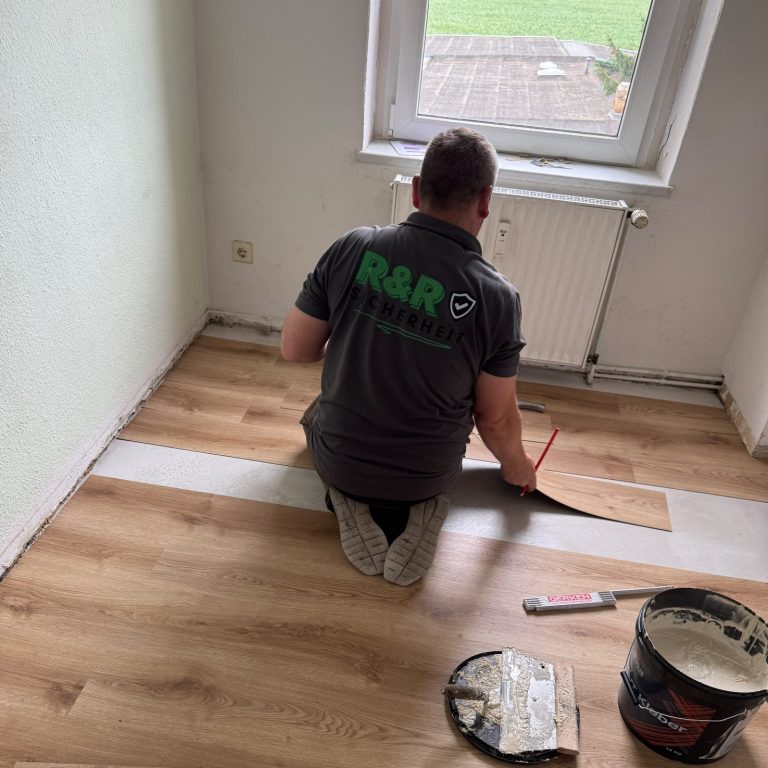 Mann verlegt Laminatboden in einem Raum mit Fenster und Werkzeugen.